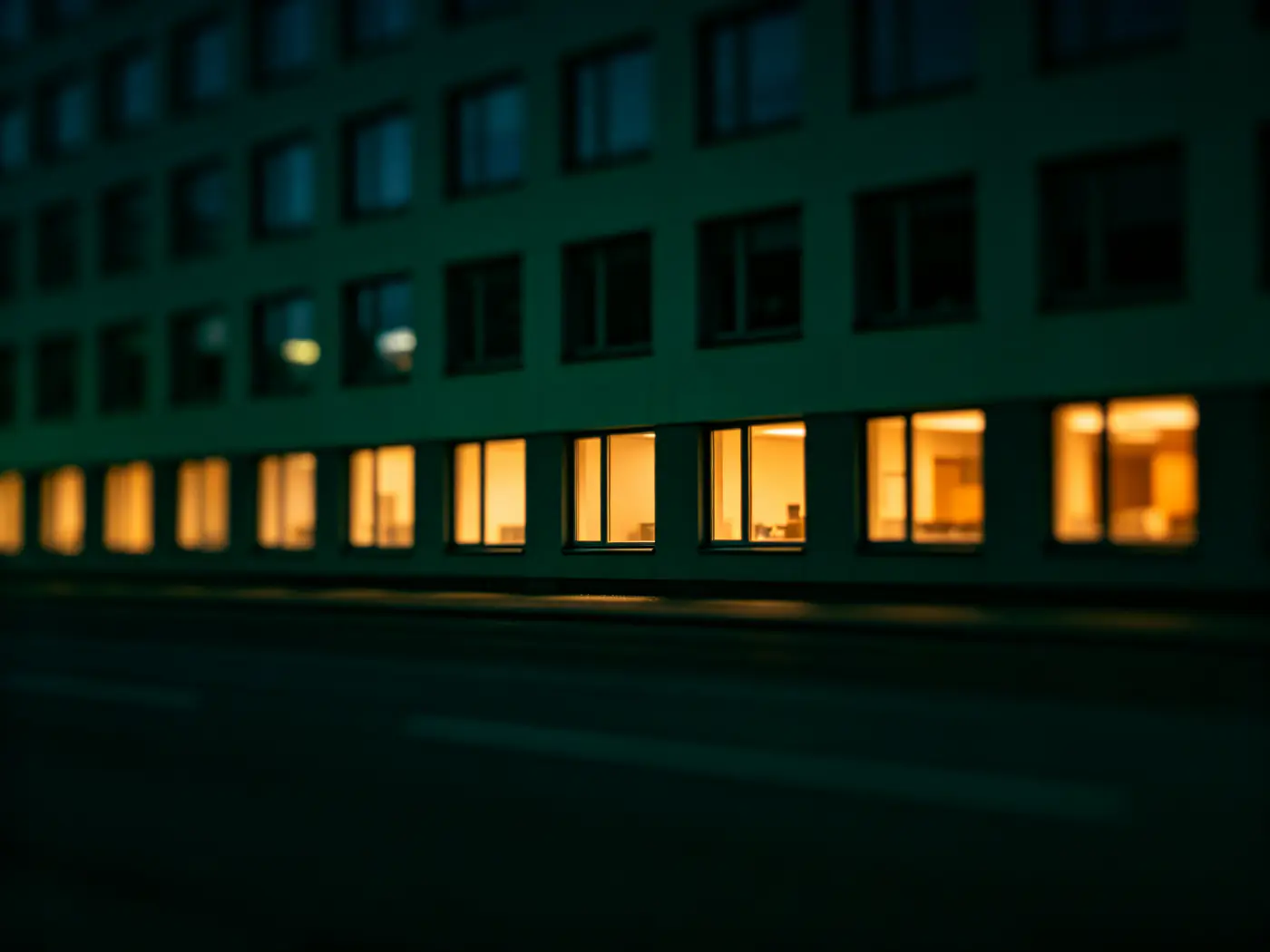En kontorsfasad i kvällsmörker med rader av upplysta fönster.